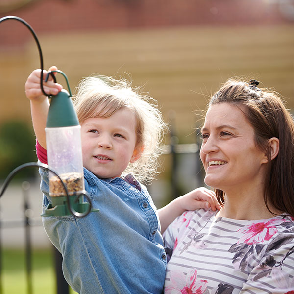 Girl hanging bird feeder with mum